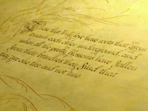 Close-up of ornate cursive poetry on aged yellow parchment, decorated with flourishes and an illuminated initial.