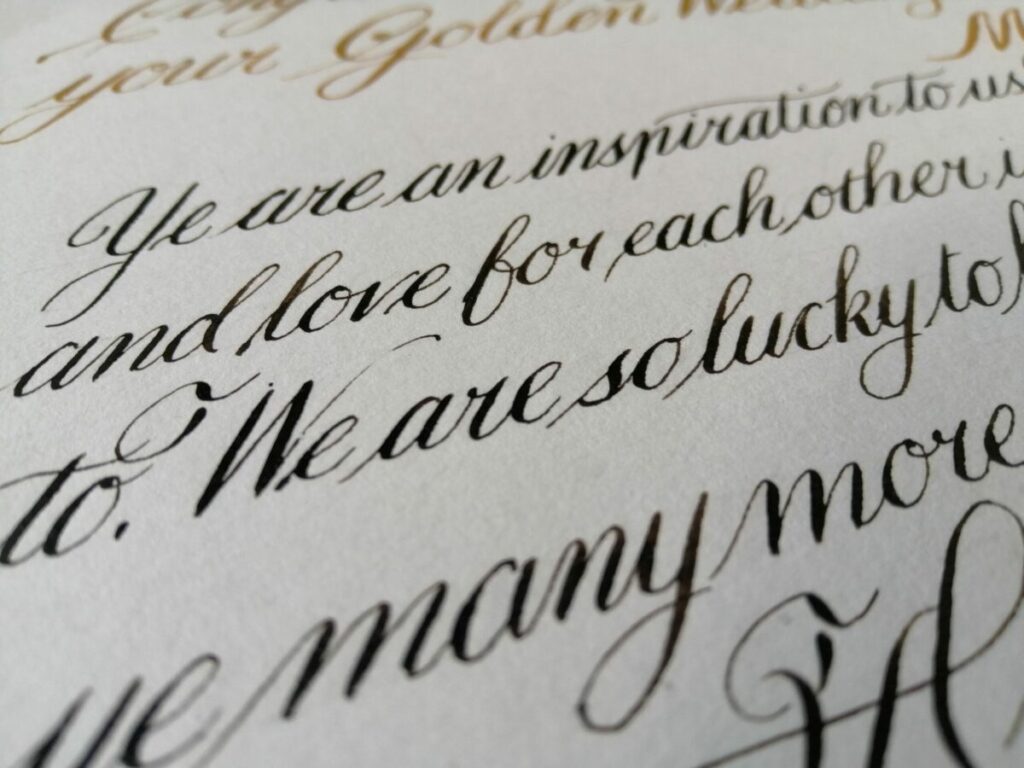 Close-up of gold and black cursive handwriting on cream-colored paper.